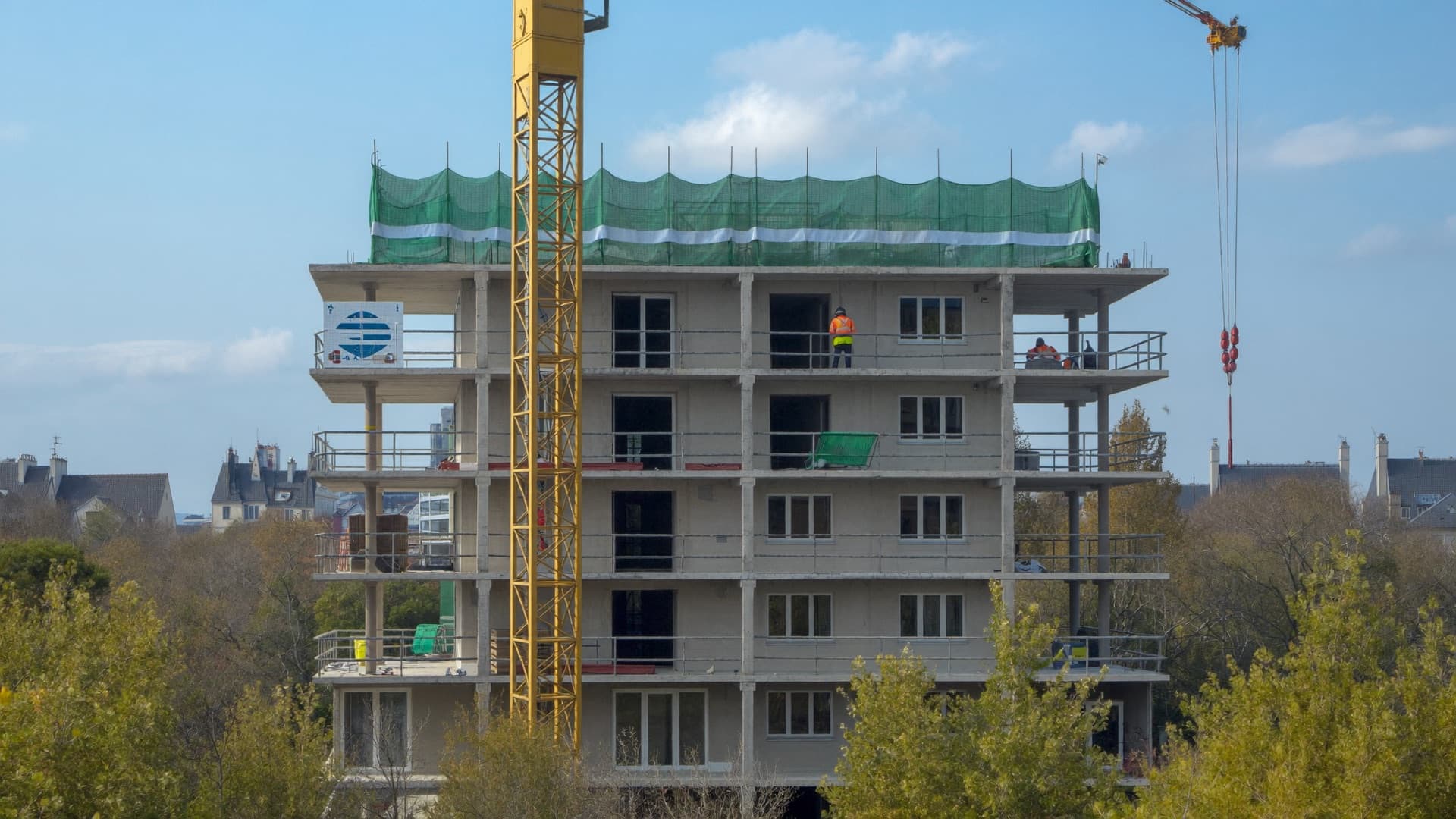 Chantier d'un immeuble de logements en France : grue à tour jaune, filets de protection et structure béton
