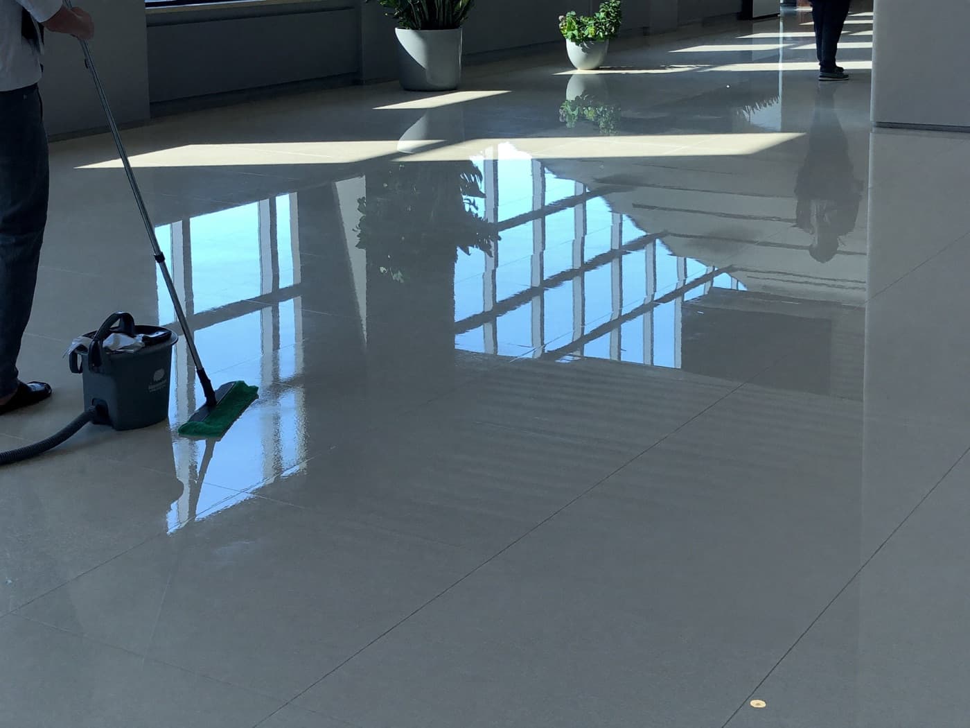 Sol d'atrium fraîchement lavé reflétant la verrière, balai microfibre et seau professionnel