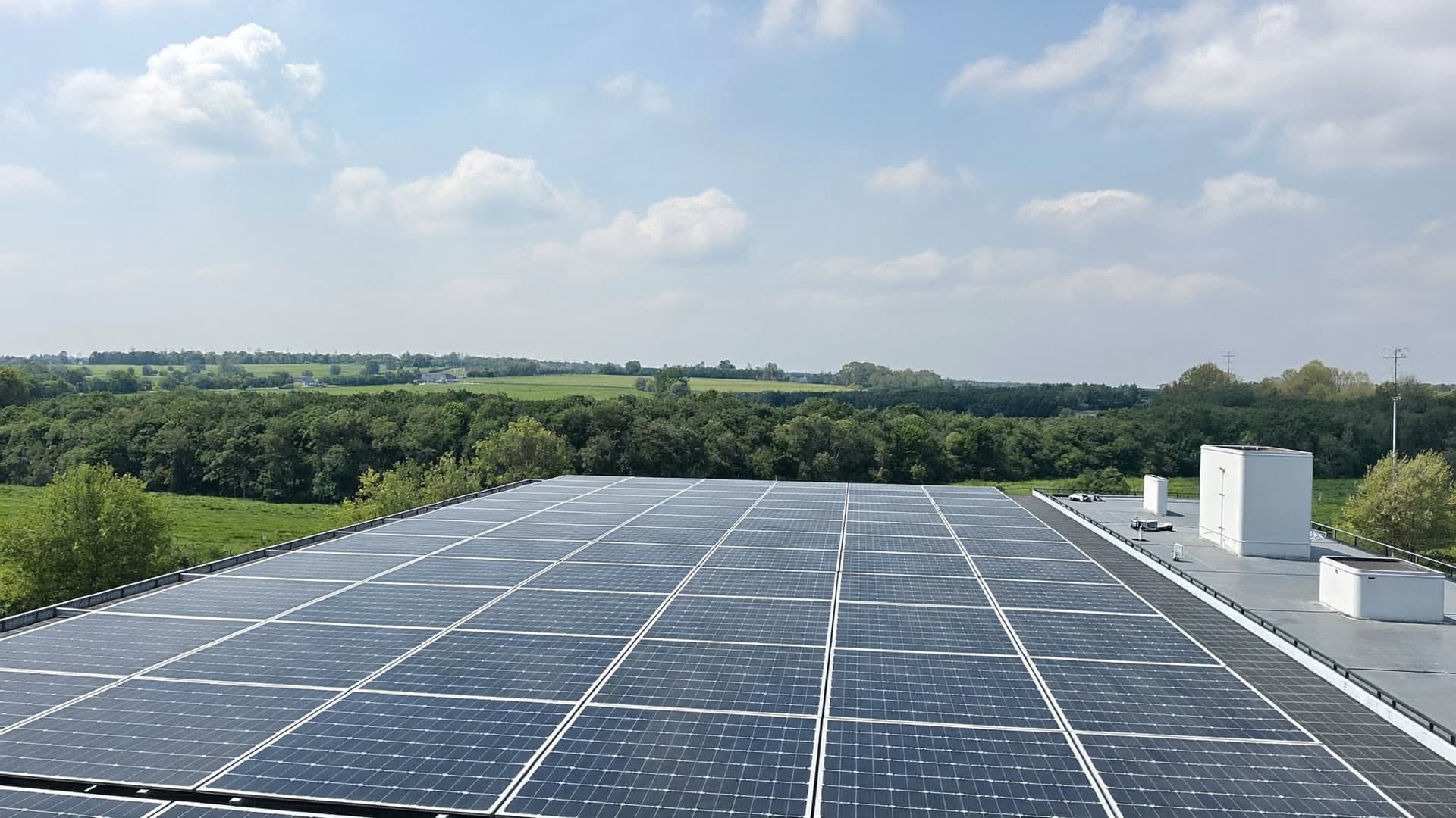 Toiture d'un bâtiment logistique couverte de panneaux photovoltaïques, campagne verdoyante au fond