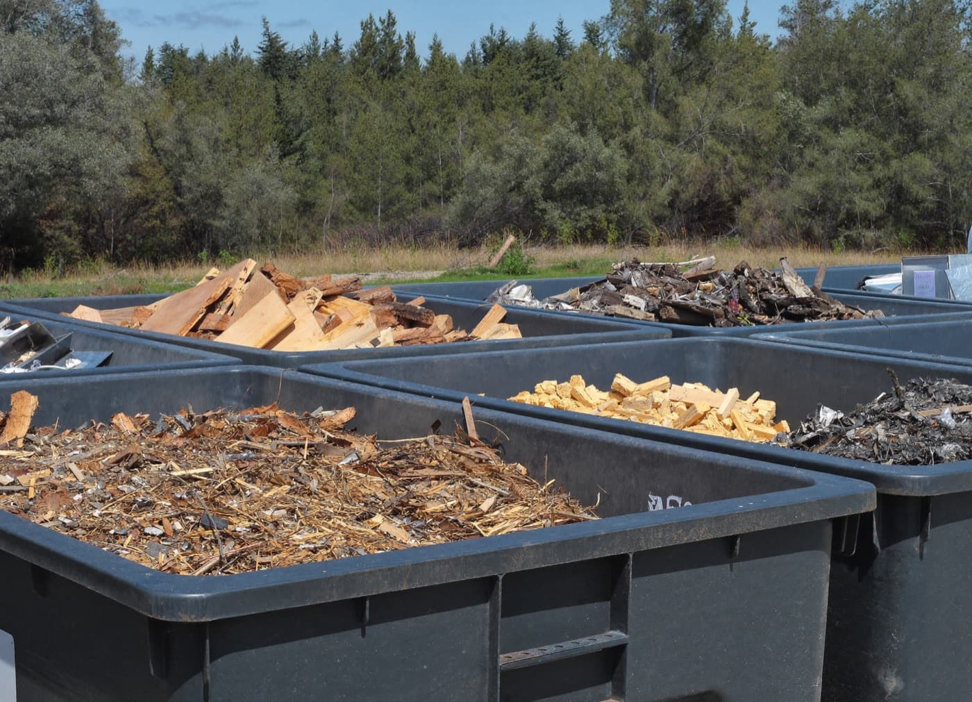 Bennes de tri sélectif de chantier séparant bois, gravats et métaux, en lisière de forêt