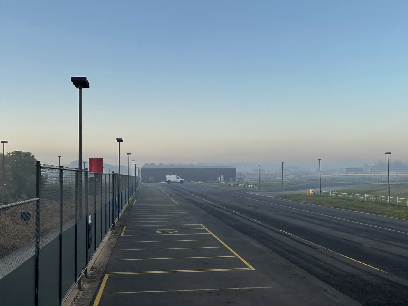 Accès clôturé et parking désert d'un site logistique à l'aube